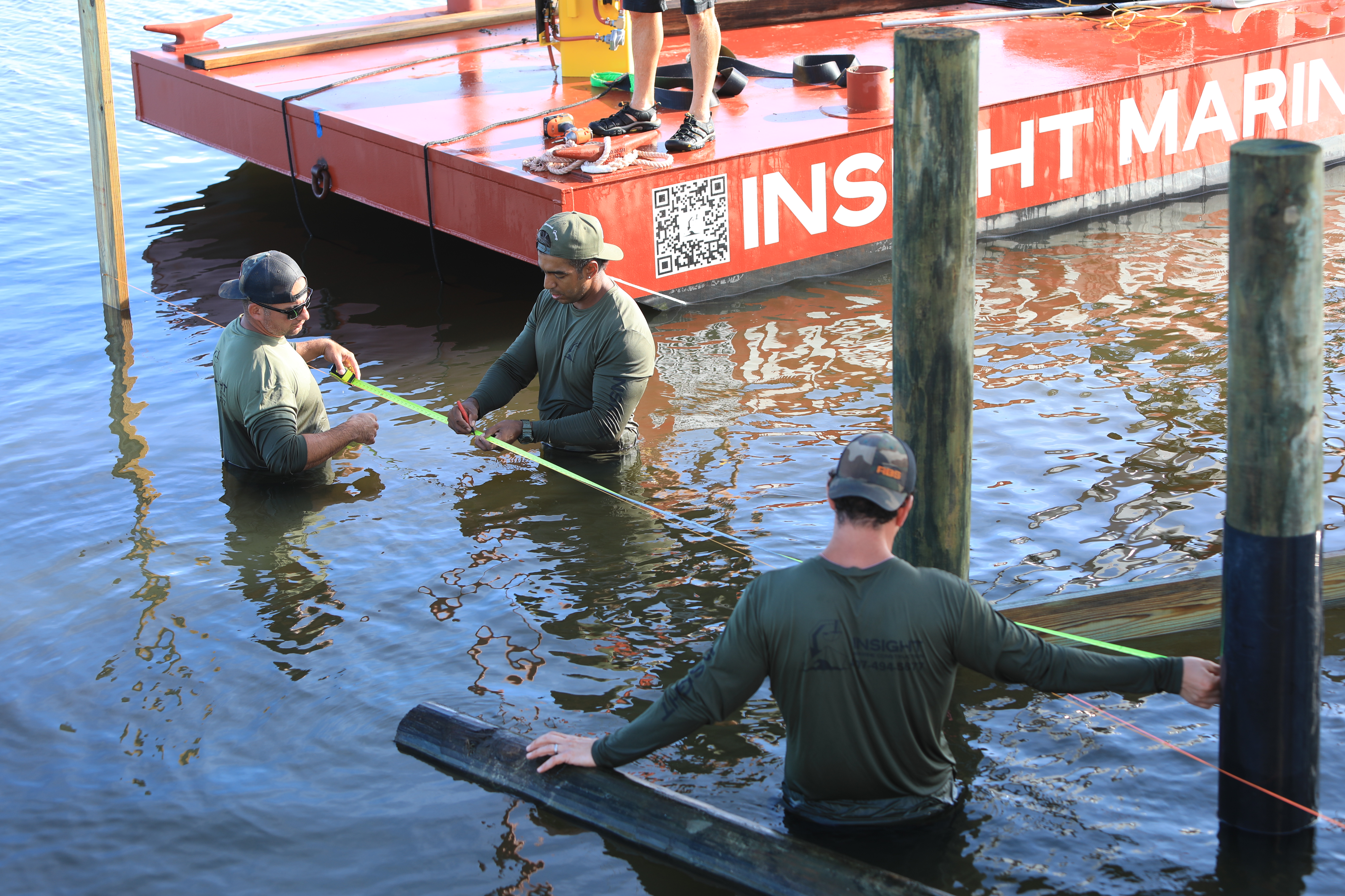 Crew waist deep in the water pulling a tape measure off the barge